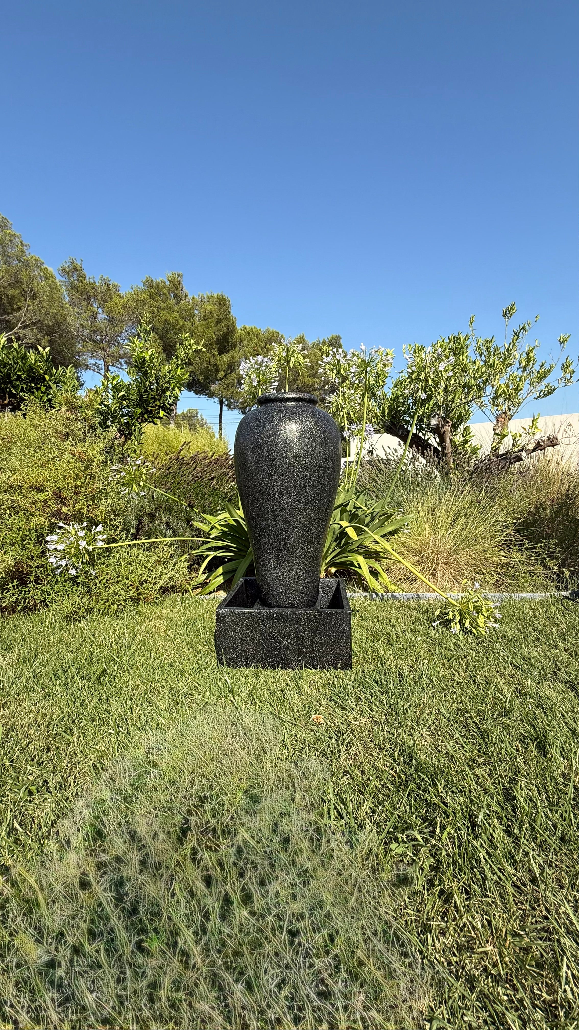 Fontaine décorative noire contemporaine de l'Ensemble Socle Noir Moderne, mise en scène dans un espace extérieur paysager.