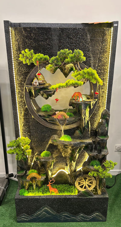 Fontaine Asiatique Dongguan éclairée en intérieur, avec détails de cerfs, maison miniature et chute d’eau, créant une atmosphère apaisante.